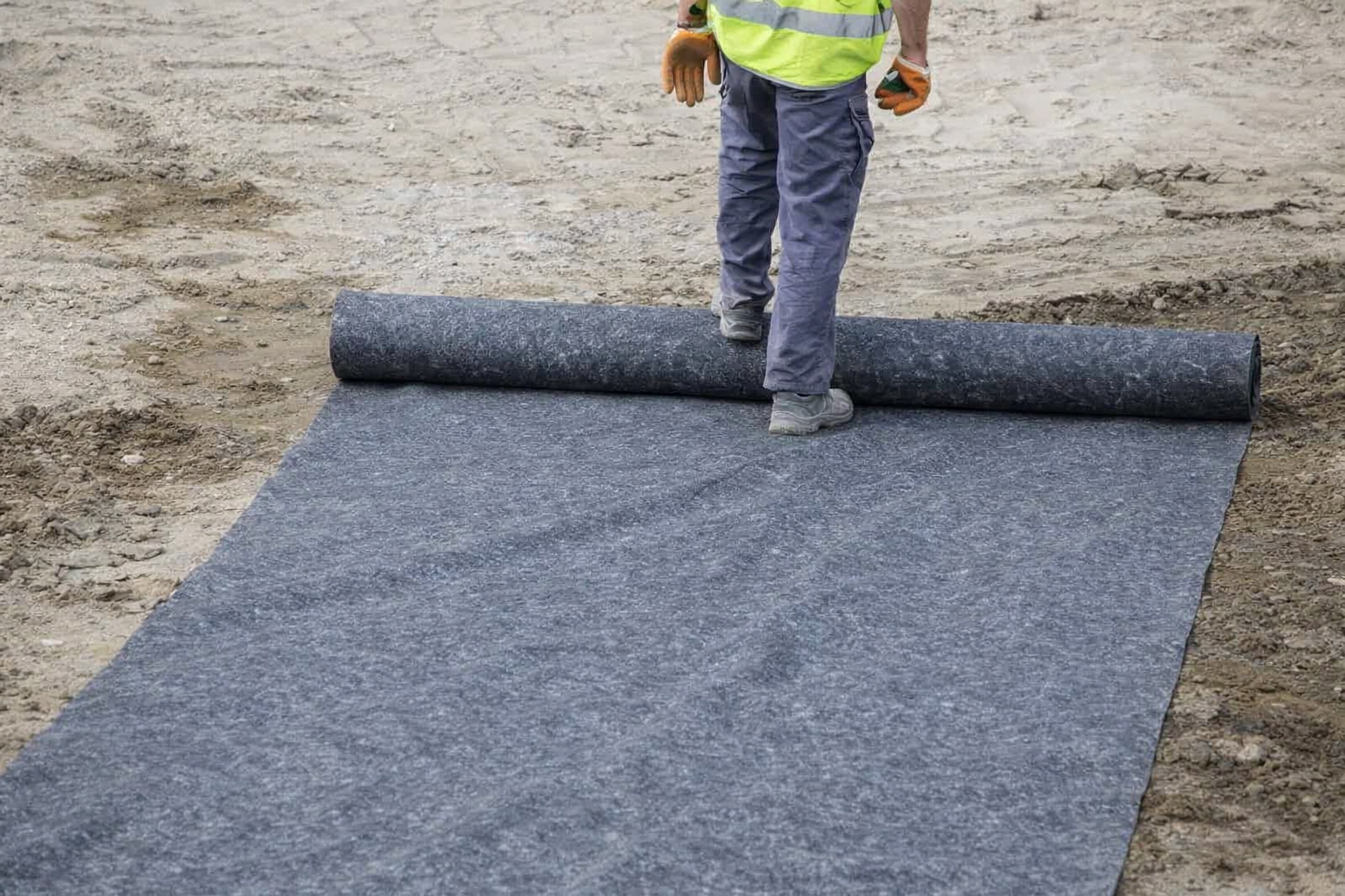 Ein Mitarbeiter rollt das Geotextil auf der Fläche aus